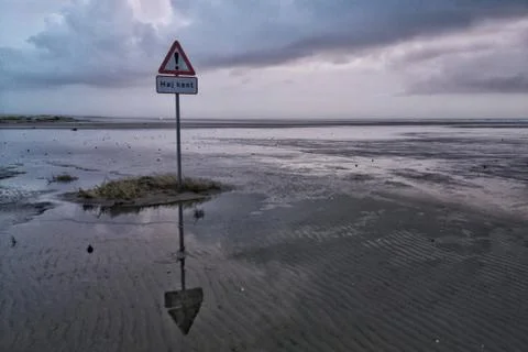 Sign on a metal pole put on the beach under a cloudy sky Stock Photos