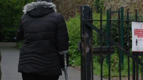 SIGN PAN TO COUPLE WALKING THROUGH PARK CORONAVIRUS COVID 19 Stock Footage 128708190