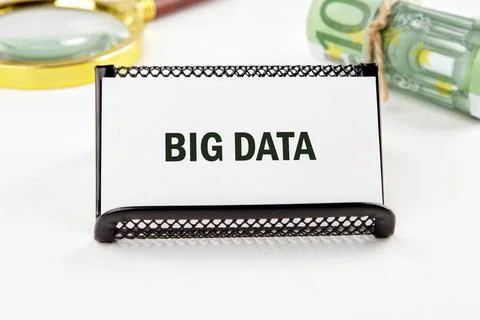 A sign reading big data is positioned on a desk alongside currency and a magn Stock Photos