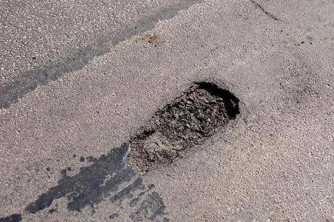 A significant pothole disrupts the smooth surface of a city street, indicat.. 库存照片