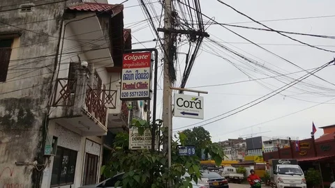 Signs underneath entangles electric cables on pole, dirty house, street, Laos 스톡 동영상 75239319