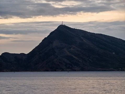 Silent peak meets tranquil waters, Remote mountain top with beacon watching over Stock Photos