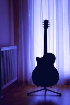 Silhouette of an acoustic guitar on a light background of curtai Stock Photos