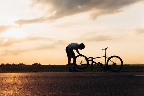 Silhouette of active man taking break for repairing bike Stock Photos