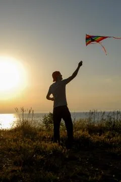 Silhouette of active young man in cap launching colorful kite flying in air at Foto stock