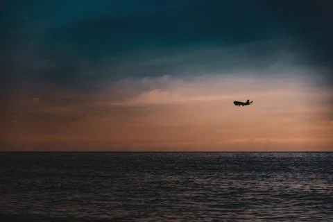 The silhouette of an airplane flies over the sea in the evening twilight. A d Stock Photos