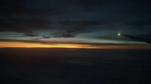 Silhouette airplane wing flying over dark clouds with sunset horizon and light Stock Footage 325050053