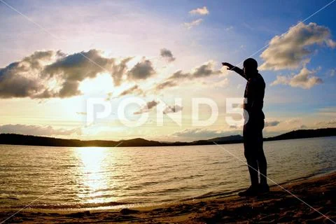 Silhouette of alone person on decline seeing over bay to sun Stock Photos