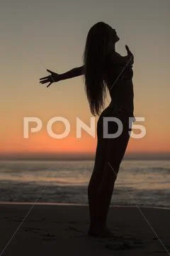 Silhouette of an attractive woman spreading her arms on the beach Stock Photos