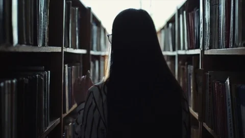 Silhouette Back view a beautiful young woman walks between the bookshelves in Stock Footage 112375451