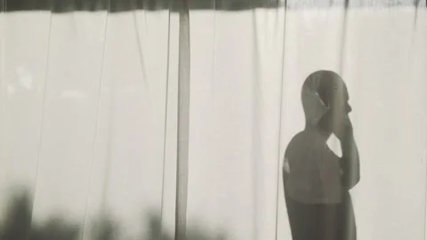 Silhouette of a bold man standing behind curtains with her smartphone Stock Footage 157284518