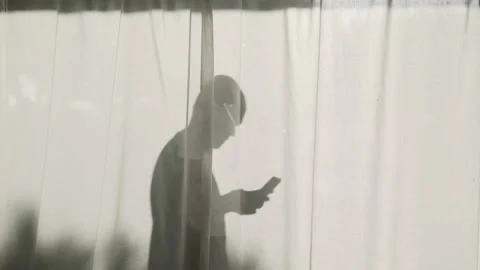 Silhouette of a bold man standing behind curtains with her smartphone Stock Footage 159281638