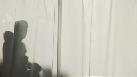 Silhouette of a bold man standing behind curtains and shakes out the towel Stock Footage 161395688