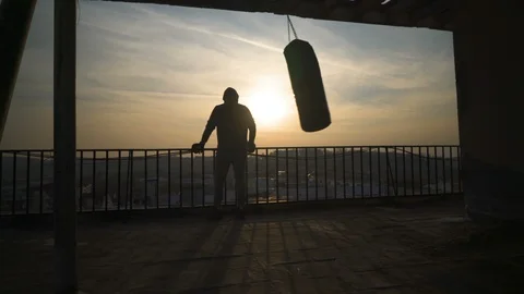 Silhouette of boxing bag while swinging, sunset, man comes and looks over fence. Stock Footage 98493630