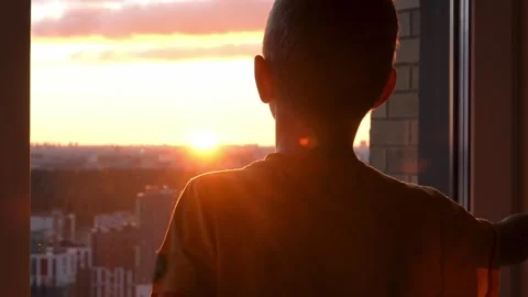 Silhouette of boy looking at sunset through window at home Stock Footage 325699524
