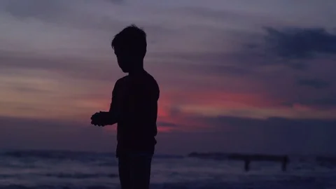 Silhouette of boy standing on beach during sunset, super slow motion 240fps Stock Footage 78559731