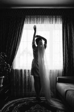 The silhouette of the bride at the window putting on her dress Fotos Stock