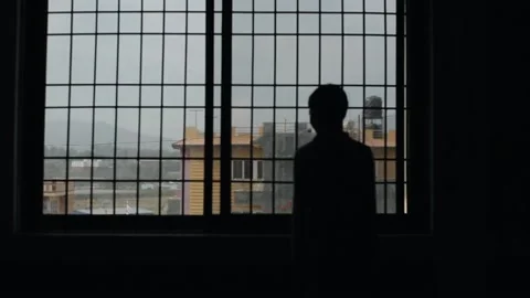 The silhouette of a brooding teenage boy in the background of a window with a 스톡 동영상 131938147