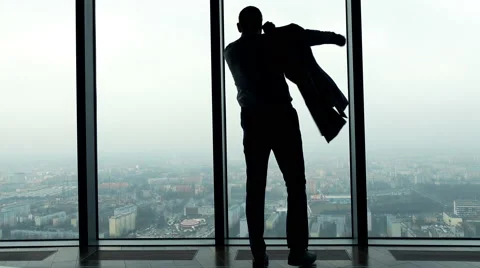 Silhouette of businessman dressing up suit jacket by the window in the office Stock Footage