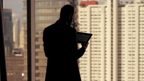 Silhouette of businessman standing with tablet computer by the window in the off Stock Footage 82261965