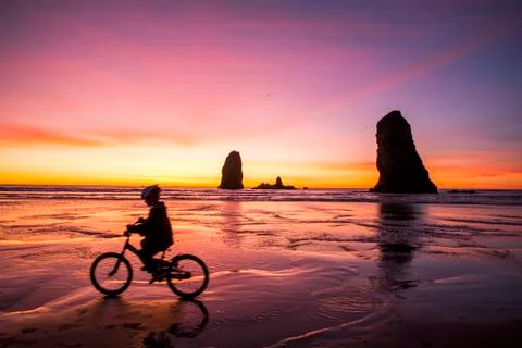 Silhouette of Caucasian girl biking near rock formations on Cannon Beach, Stock Photos