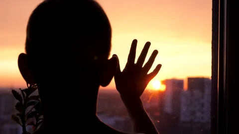 Silhouette of a child looking at the sunset through a window put arm on glass Stock Footage 339629082