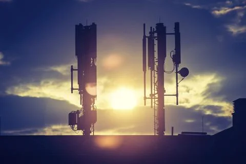 Silhouette of communication or cell tower on the rooftop of a building, evening Stock Photos