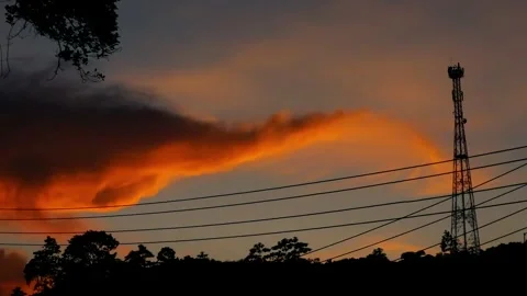 Silhouette of communication tower and power lines against a dramatic orange 動画素材 332984634