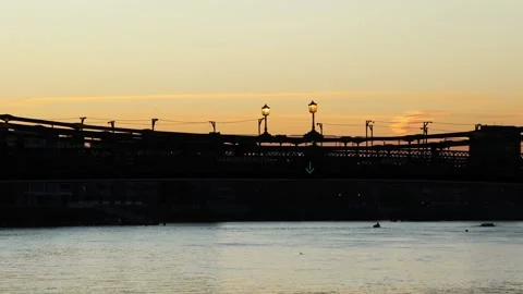 Silhouette of commuters crossing Hammersmith Bridge at sunrise. Zoom out Stock Footage 166951491