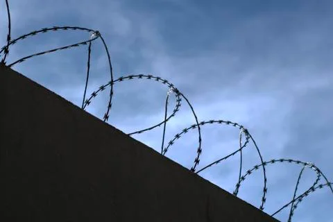 Silhouette of concertina wire perimeter over a wall Stock Photos