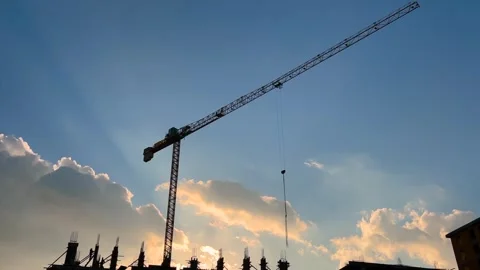 Silhouette of construction crane moving over construction site at sunset Stock Footage 346544104