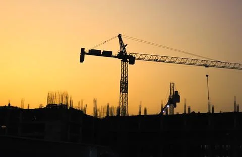 Silhouette of construction cranes and orange sky at dusk. Stock Photos