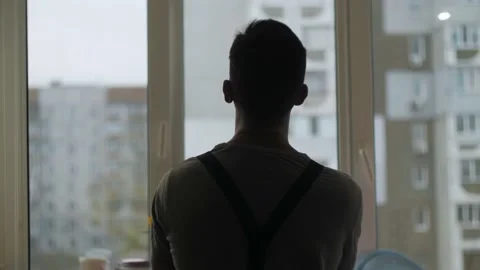 Silhouette construction worker stands by the window takes off helmet.Handyman Stock Footage 220833838
