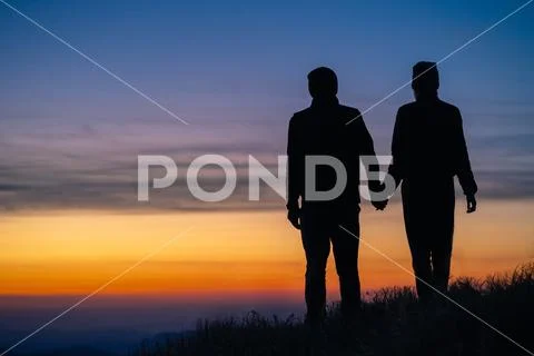 The silhouette of the couple on the mountain with a sunrise background Stock Photos