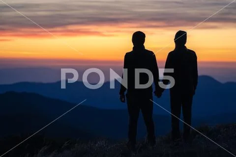 The silhouette of the couple on the mountain with a sunset background Stock Photos