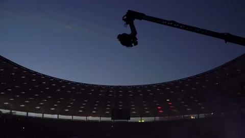 Silhouette of a crane with a video camera in a stadium shoots a concert Stock Footage 112864306