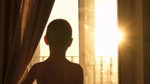 Silhouette of curious boy opening curtains at sunrise Stock Footage 325119981