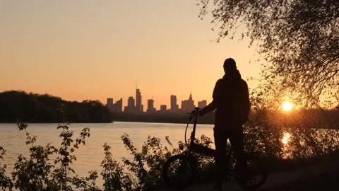 The silhouette of a cyclist against the backdrop of evening Warsaw. A big city Stockbeeldmateriaal 240216385