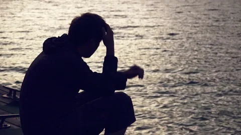 Silhouette of depressed sad man sitting by the lake Stock Footage