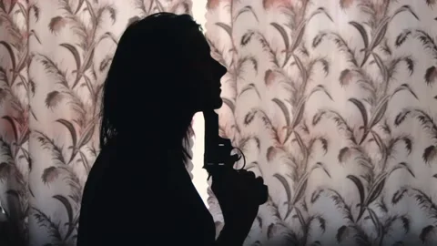 Silhouette of depressive woman trying to commit suicide with gun near the window Stock Footage 200775276