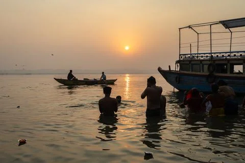 Silhouette of devotees bathing in holy river with boat at sunrise Stock Photos