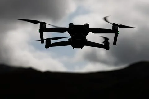 Silhouette drone flying against dramatic cloudy mountain sky Stock Photos