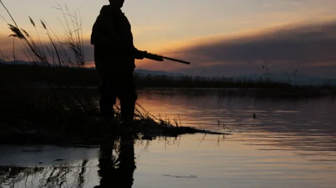 Silhouette of a duck hunter standing on the lake Stock Footage
