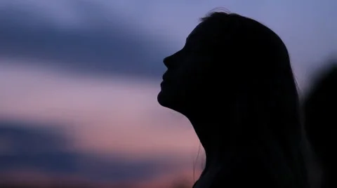 Silhouette at dusk of young girl prayer praying looking up at sky Stock Footage