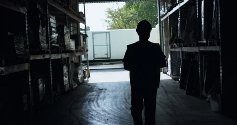 Silhouette of engineer walking between shelves in a warehouse to entrance Stock-Footage 128048861