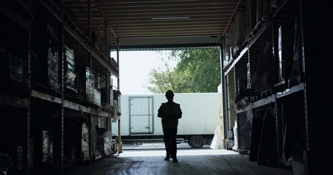 Silhouette of engineer walking to camera between shelves in a warehouse 스톡 동영상 127813024