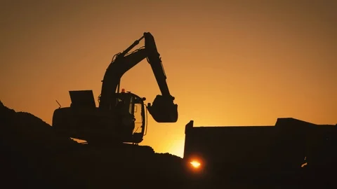 Silhouette of an excavator that loads sand into a truck at sunset. Concept Stock Footage