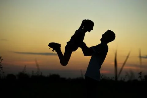 Silhouette of father throwing up his happy daughter in the air at sunset. Stock Photos