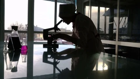 Silhouette of a female assistant looking through a microscope against light from Stock Footage