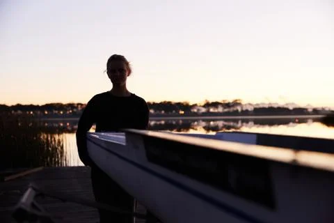 Silhouette of female rower lifting scull on sunrise lakeside dock Stock Photos